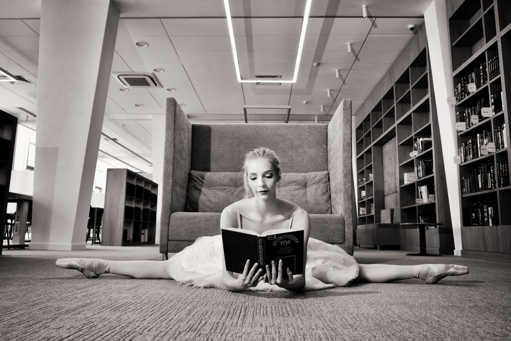 der Träumer. Ballerina auf Spitzenschuhen in der Bibliothek liest ein Buch und hält es hoch von Alexandr