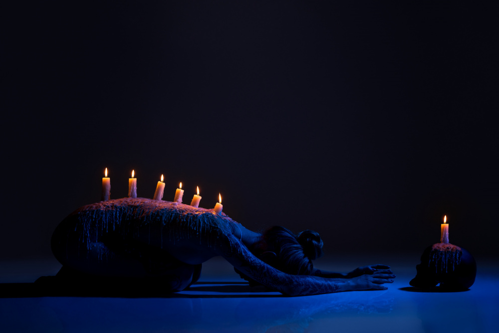 Brennende Kerzen auf dem Rücken einer Dame,die sich in der Dunkelheit verneigt von Andrey Guryanov
