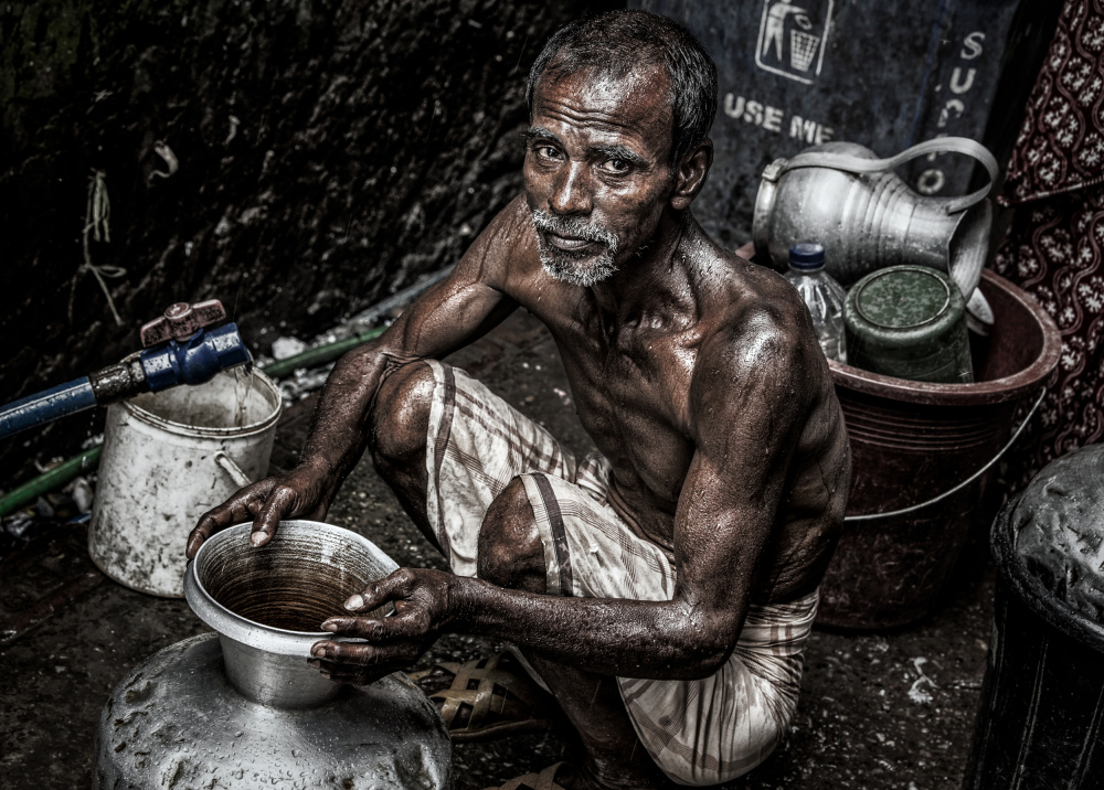 Mann füllt einen Krug mit Wasser in den Straßen von Bangladesch. von Joxe Inazio Kuesta Garmendia